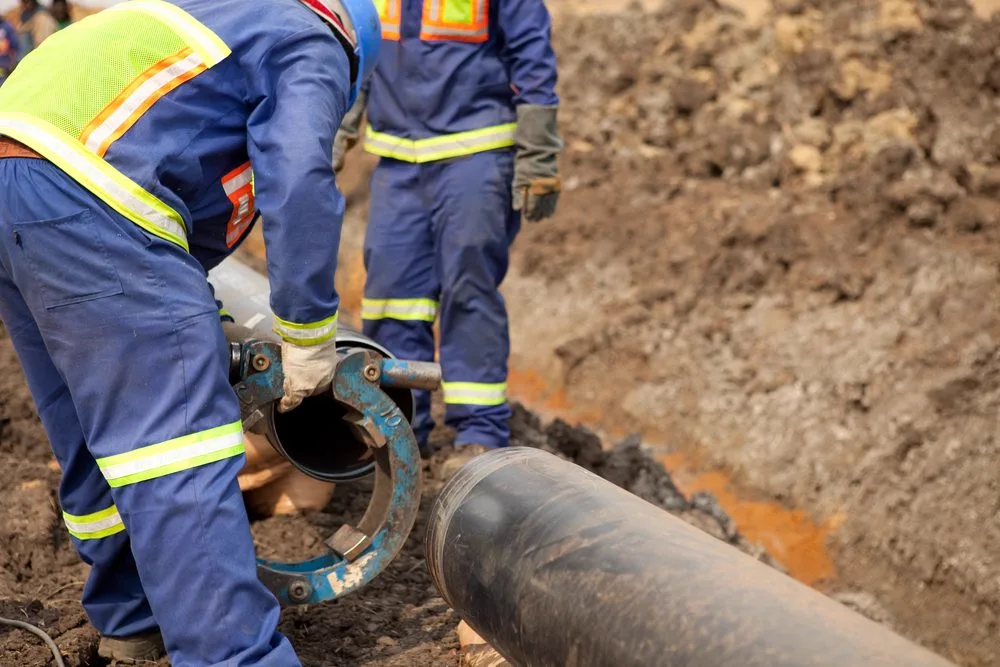 Two licensed drainers working together on an underground drain pipe in a trench