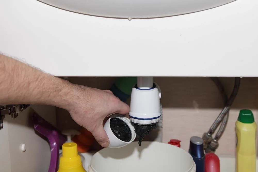 Plumber pulling apart a blocked sink trap with a bucket underneath to clear the blockage