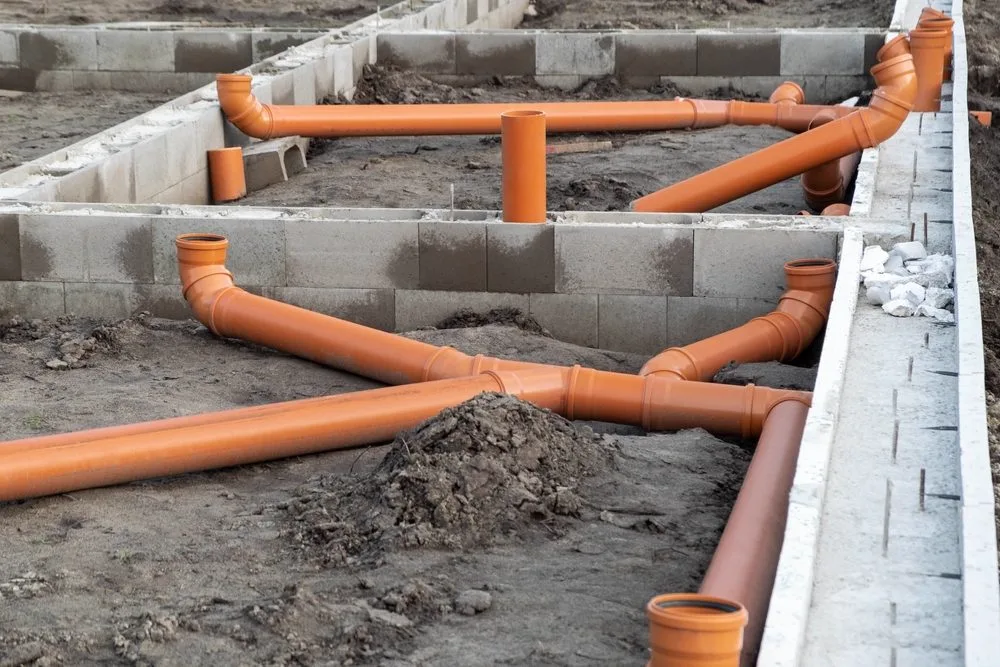 New orange PVC drain pipework set out against a concrete slab during a drain upgrade