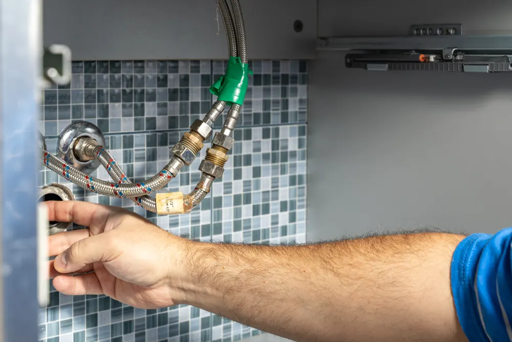 Plumber tightening drainage pipe connections behind a wall panel