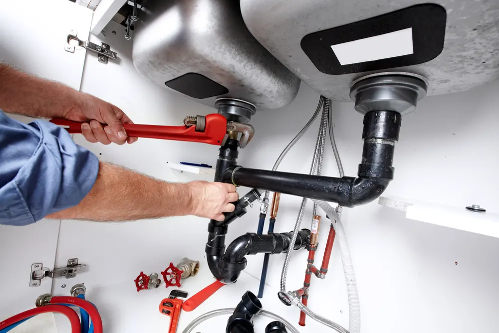 Drainer working on blocked sink waste pipework with hand tools