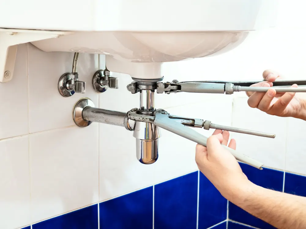 Plumber clearing a blocked waste trap under a bathroom basin