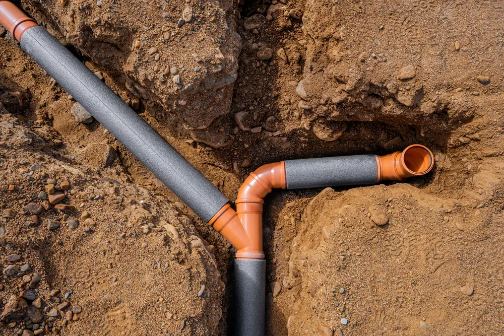 Buried drain pipe junction uncovered in soil while locating and inspecting a drain line