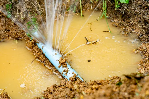 Water spraying from a broken underground pipe in muddy ground before repair