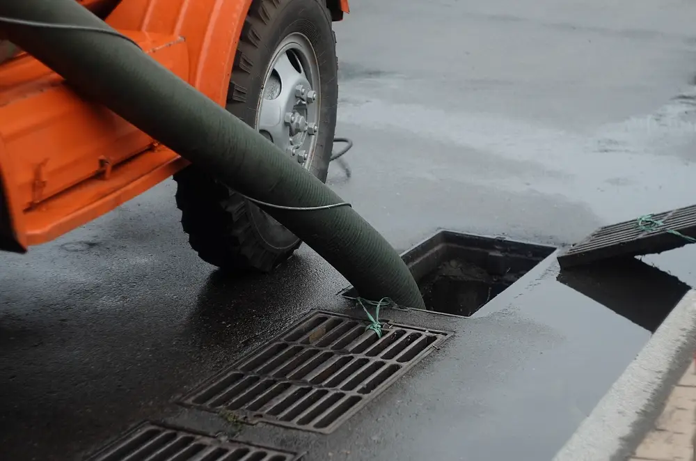 Drainage truck vacuum hose fed into a street drain grate during a drain inspection