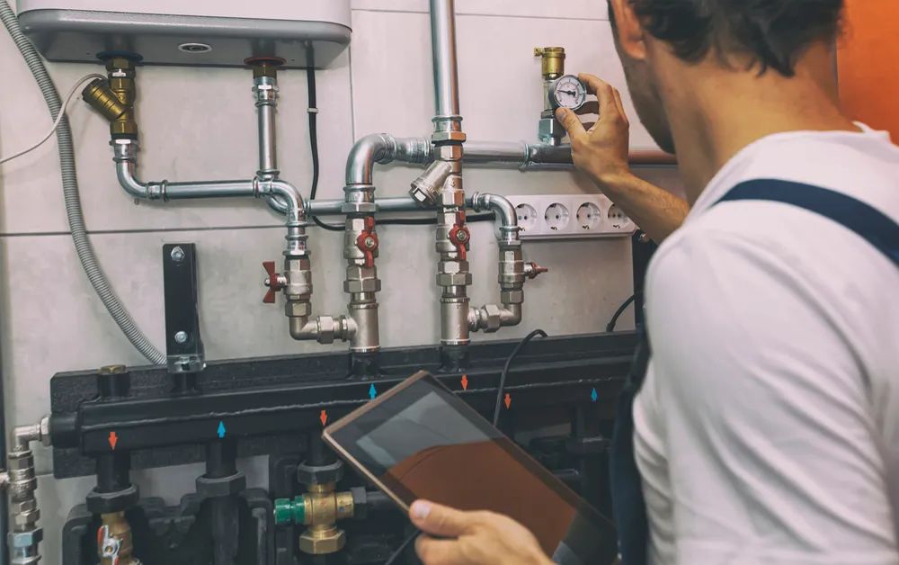 Drainage technician reviewing CCTV drain inspection footage on a tablet beside pipework